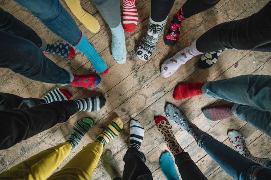 A circle of feet in colourful socks on a wooden floor — different, together.